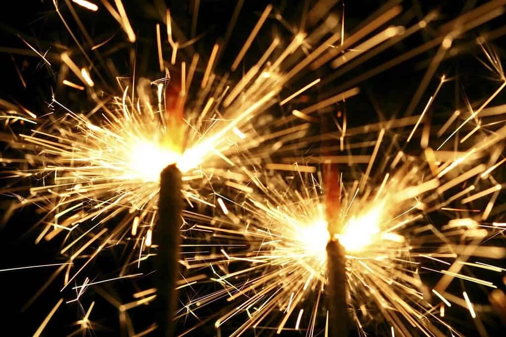 Bright sparklers emitting golden sparks on a dark background, symbolizing celebration and energy.