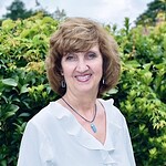 Judy Christopher smiling outdoors with greenery background.