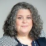 Professional business woman with curly gray hair in a modern office setting.