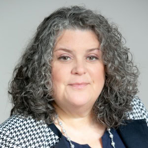 Professional business woman with curly gray hair in a modern office setting.