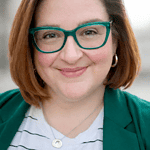 Confident woman with glasses smiling outdoors, professional headshot.
