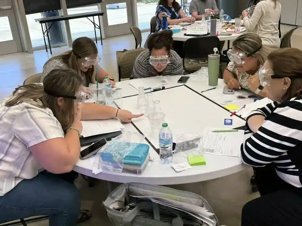 Team Collaboration in Laboratory Setting Group of women wearing safety goggles working together at a round table.